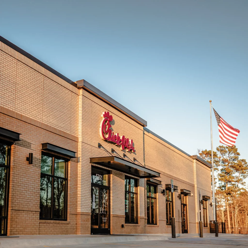 Exterior of a Chick-fil-A restaurant with large windows, brick facade, an American flag; Scott Systems installed efficient commercial kitchen ventilation on the interior.
