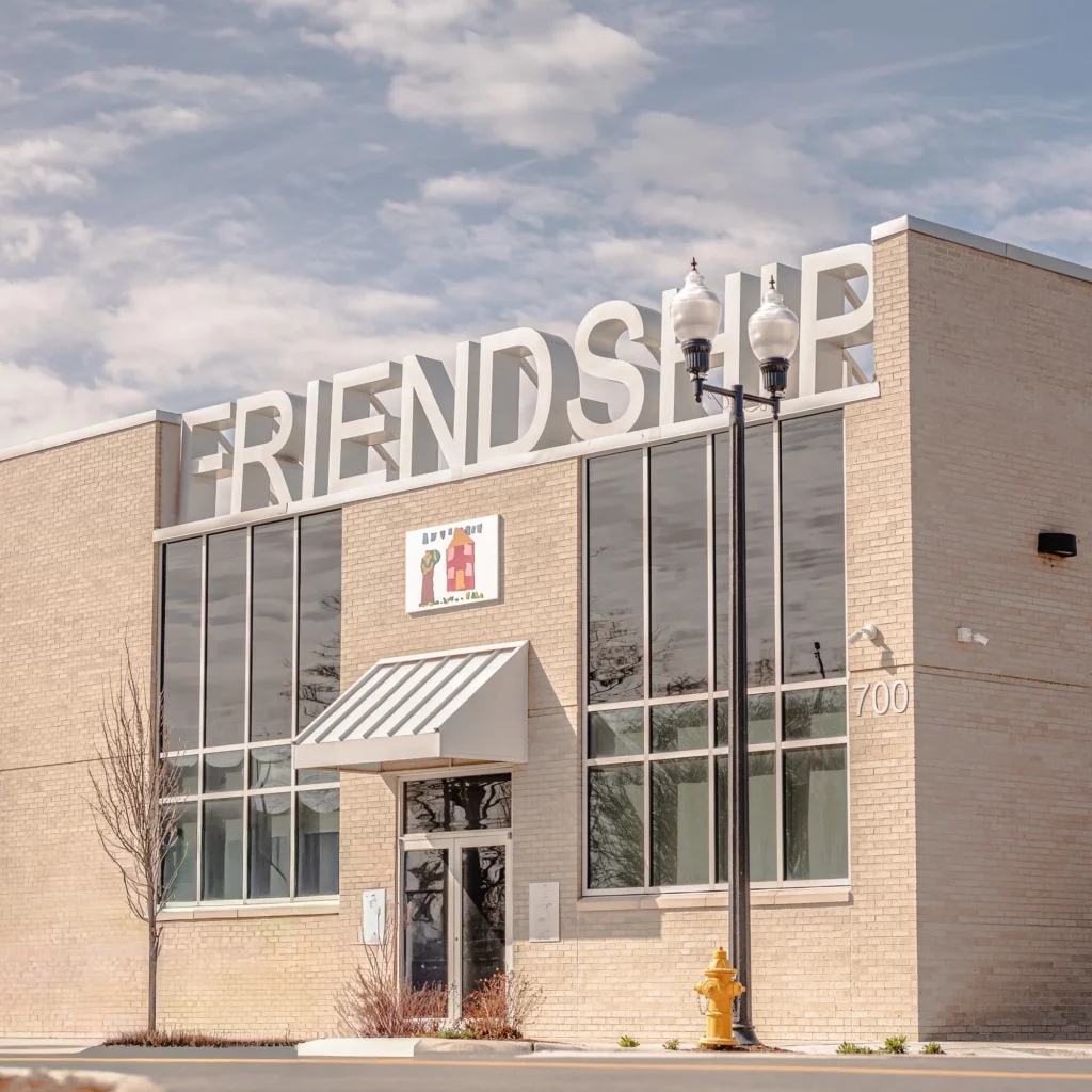 A beige brick building with large glass windows and FRIENDSHIP in large letters on the roof.